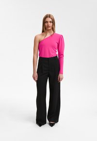 Enganliegender einseitiger Top in leuchtendem Pink mit puffigem Ärmel; kombiniert mit hochgeschnittenen schwarzen Hosen und spitzen schwarzen Absätzen.
