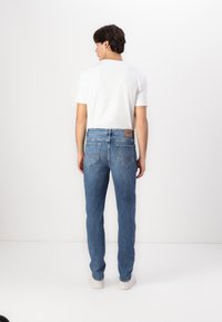 Faded blue denim jeans with a straight leg design, featuring a brown leather patch on the back waistband and double-stitched pockets.