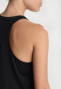 Top da allenamento nero senza maniche con design a schiena scoperta, caratterizzato da un tessuto morbido, cuciture minime e una schiena aperta che rivela il tono della pelle.