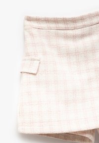 Valkoiset tweed-lyhyet housut, joissa on hienovarainen vaaleanpunainen ruutukuosi. Housuissa on sivutasku, rakenteellinen vyötärö ja teksturoitu pinta.