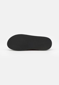 Black rubber shoe sole with a smooth surface and textured grooves for grip. Rounded shape with a slight curve at the heel area.
