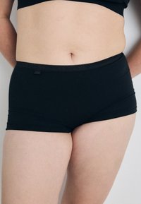 Svarta stretchiga bomullshipsterunderkläder med ett slätt midjeband och minimala sömdetaljer, med en etikett på midjebandet.