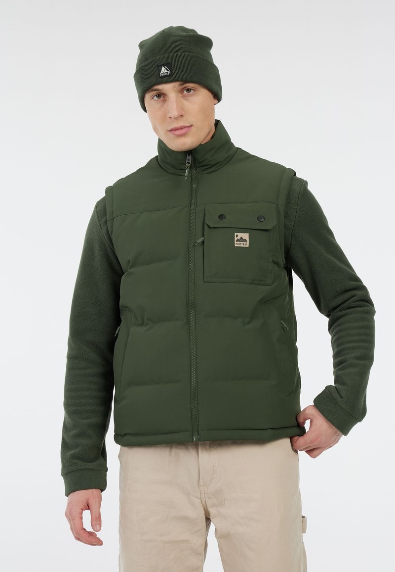 Groene puffer gilet met een rits aan de voorkant, gewatteerd ontwerp, borstzak en logo patch. Draagt over een groene fleece top, gecombineerd met beige broek.