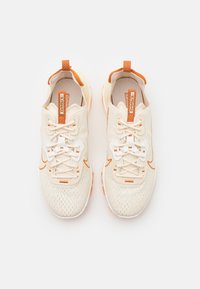 Baskets de sport beige clair avec des accents orange, tige en mesh et lacets blancs contrastants. Présentent une langue rembourrée et une semelle en caoutchouc.