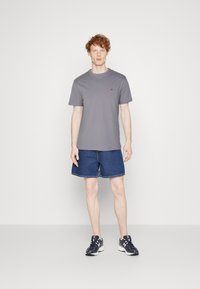 Grå kortermet t-skjorte med en liten rød logo, sammen med blå denimshorts og svarte joggesko. En enkel, uformell antrekk.