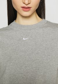 Grå bomullströja med rundad hals och korta ärmar, med en liten vit Nike-logotyp på bröstet. Slät textur.