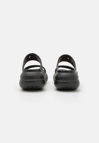 Črne gumijaste obuvale z odprtimi petami, nastavljivimi trakovi in teksturiranimi podplati, ki jasno prikazujejo logo "CROCS".