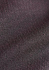Tissu textile présentant une surface texturée et côtelée avec des teintes violettes foncées et noires, affichant des variations subtiles et des détails fins.