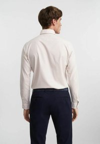 Jasnoróżowa koszula w kratkę z długimi rękawami, zapinanym kołnierzykiem i kontrastującymi niebieskimi spodniami. Wyróżnia się luźnym krojem i gładką fakturą.