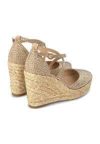 Beige wedge sandals with decorative rhinestones, strappy design, a braided jute outsole, and a smooth matte finish on the upper.