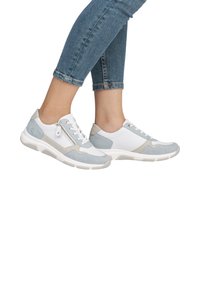 Chaussures de sport blanches et gris clair avec texture en maille et en daim, dotées d'une fermeture éclair sur le côté et d'une semelle épaisse, présentées avec un jean en denim.