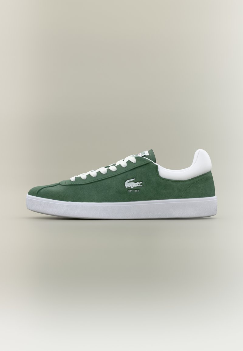 Χαμηλού προφίλ πράσινα σουέτ αθλητικά παπούτσια με λευκές κορδόνες, λευκή σόλα, μαξιλαρωμένο κολάρο στον αστράγαλο και κεντημένο λογότυπο κροκοδείλου με το κείμενο "ΙΔΡΥΘΗΚΕ 1933".