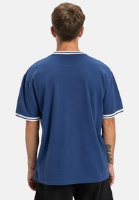 Modrá krátkymi rukávmi tričko s bielymi pruhmi na golieri a rukávoch; vyrobené z hladkej, priedušnej látky.