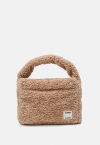 Sac à main flou, beige, avec une surface douce et texturée et une poignée arrondie. Présente une étiquette de marque visible à l'avant.
