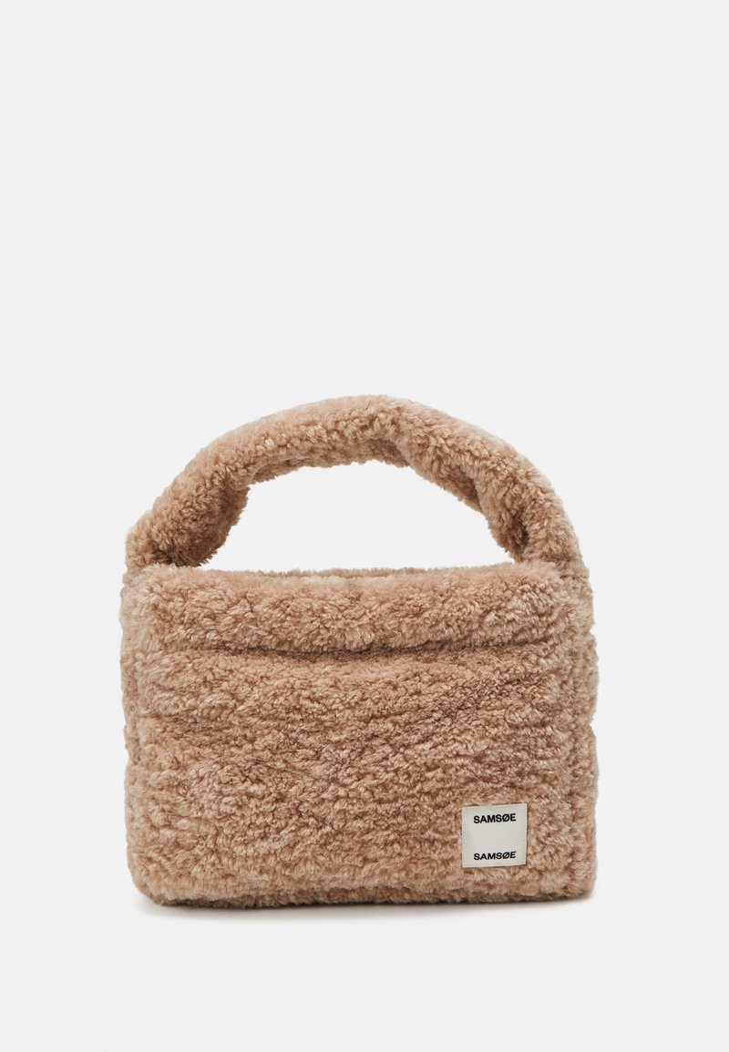 Sac à main flou, beige, avec une surface douce et texturée et une poignée arrondie. Présente une étiquette de marque visible à l'avant.