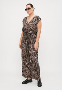 Jumpsuit s tkanino z leopardjim vzorcem, ki je lahkotna, z globokim V-izrezom, kratkimi rokavi in pasom s pripenjanjem. Črne loafer čevlje dopolnjujejo videz.