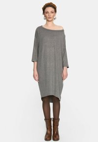 Szara sukienka opuszczająca ramiona z rękawami o długości trzy czwarte, miękka tekstura, do kolan, charakteryzująca się luźnym krojem, w połączeniu z brązowymi botkami za kostkę i rajstopami.
