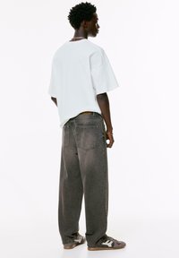 T-shirt blanc oversize, coupe décontractée. Jean baggy gris avec poches arrières, porté avec des baskets basses présentant des rayures et des accents texturés.