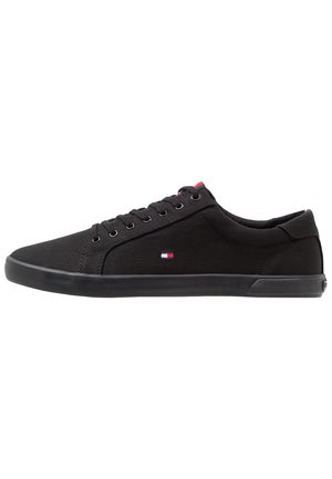 Zwarte canvas sneakers met een rubberen zool, voorzien van zilveren oogjes en een klein rood, wit en blauw logo aan de zijkant. Vetersluiting.