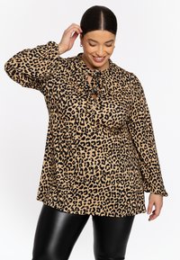Bluse im Leopardenmuster in Beige und Schwarz, mit hochgeschlossenem Kragen und Bindeband, langen Ärmeln; glattes Material, lockere Passform.