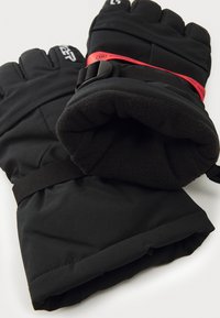 Guantes aislantes negros con una capa exterior texturizada, dedos curvados, correa de acento roja y forro interior suave para mayor calidez.