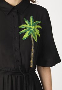 Rochie neagră cu guler, cu un grafic de palmier verde; mâneci scurte, deschidere cu nasturi și detaliu cu cordon la talie. Textură de material moale.