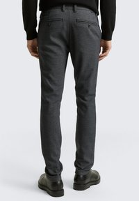 Dark gray, slim-fit trousers in a textured fabric. Back features two pockets with button closures. Worn with black ankle boots.