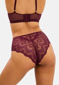 Spets hipster-trosor i djup burgunderröd med intrikata blommönster, vågiga kanter och ett mjukt, genomskinligt midjeband.