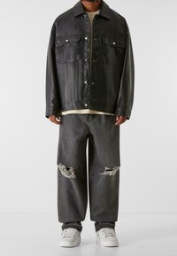 Czarna skórzana kurtka z dwoma przednimi kieszeniami i srebrnymi napami, zestawiona z podartymi szarymi dżinsami i białymi trampkami. Pod spodem gładka koszulka.