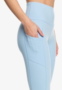 Lichtblauwe high-waisted leggings van rekbaar materiaal, met een zijzak en naadloos ontwerp met zichtbare stiksels.