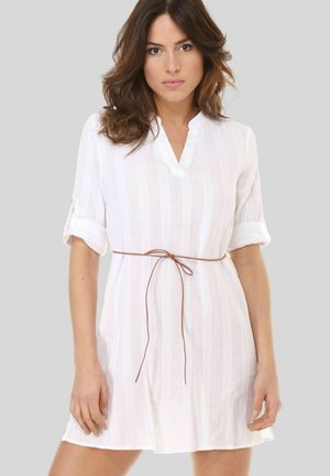 Vestido blanco con una tela texturizada, que presenta un escote en V y mangas enrolladas. Un cinturón de lazo marrón resalta la cintura.