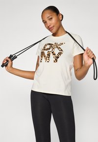Krémové tričko s logo "DKNY" v leopardom vzore, krátke rukávy, okrúhly výstrih, kombinované s čiernymi legínami, s preskakovaním švihadla.