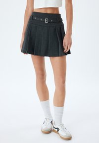 Grå plisseret mini nederdel med bælte i taljen, metalhardware accenter og en glat tekstur. Kombineret med hvide sokker og sneakers.