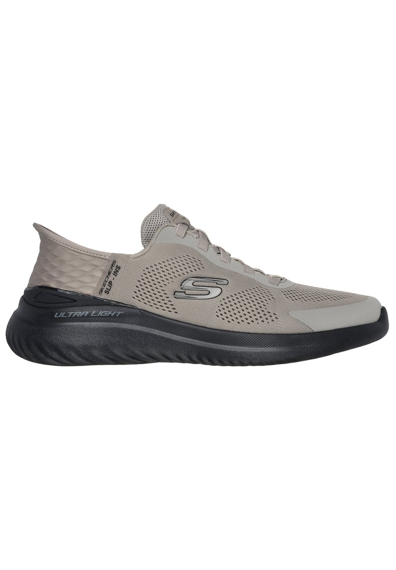 Zapatilla deportiva ligera de color gris con parte superior de malla, cuello texturizado y suela de goma negra. Presenta un diseño sin cordones y un detalle de logo en el costado.