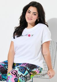 T-shirt blanc à manches courtes avec un design graphique coloré représentant un visage souriant. Associé à des leggings à motifs multicolores.