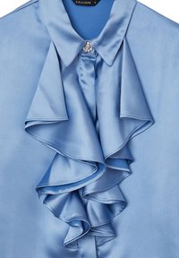 Himmelblaue Satinbluse mit gerafftem Vorderteil, spitzem Kragen und einem dekorativen Edelsteinelement am Ausschnitt. Glatte Textur über die gesamte Bluse.