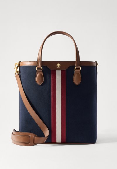 Sac fourre-tout en toile marine avec des accents en cuir marron, featuring une bande centrale rouge et blanche, des anses supérieures et une bandoulière amovible.