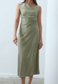 Robe en satin vert avec un design asymétrique à une épaule, des détails drapés et une longueur au genou. Texture lisse et silhouette ajustée.