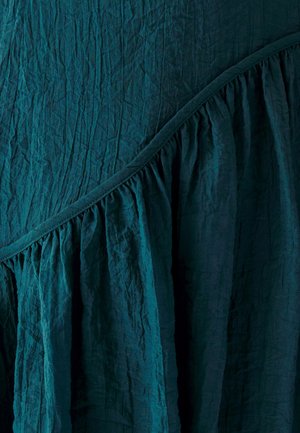 Tkanina w kolorze turkusowym o pomarszczonej fakturze ma ukośny falbanek wzdłuż szwu, co dodaje wymiaru projektowi. Miękki, lekki materiał.