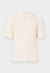 Camisa polo de manga corta color crema con un patrón de punto texturizado, con cuello acanalado y tres botones en la parte frontal.