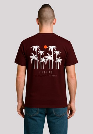 Maroon cotton t-shirt featuring a white palm tree graphic, red sun, and text "ESCAPE AND DISCOVER THE WORLD" on the back.