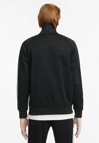 Giacca sportiva nera con colletto alto, caratterizzata da una texture liscia e strisce bianche a contrasto lungo le maniche. Polsini e orlo elastici.
