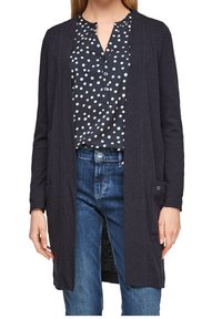 Marinblå lång kofta med öppen front, två sidofickor och långa ärmar, bärs över en vit blus med prickar och blå jeans.