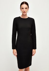 Abito lungo nero a maniche lunghe con silhouette aderente, scollatura rotonda e orlo fino al ginocchio. Tessuto morbido e dettagli di cucitura sottili.
