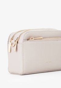 Beauty case di un beige chiaro con finitura testurizzata, dotata di due chiusure lampo in tonalità oro e una tasca frontale, forma rettangolare.