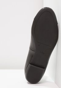 Suola di una scarpa elegante in pelle nera con tacco basso, che mostra il battistrada e il nome del marchio "hōgl" su uno sfondo bianco semplice.