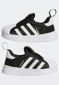 Černé sneakers na slip-on s bílou gumovou špičkou a třemi bílými pruhy. Texturovaný svršek a poutko na zadní straně. Bílá podrážka.