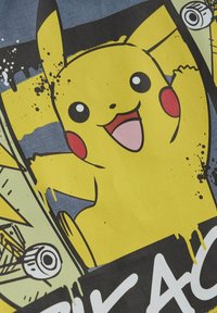 Gelbes Baumwoll-T-Shirt mit einem Grafikmotiv eines lächelnden Pikachu vor einem blau-schwarzen Hintergrund, ergänzt durch abstrakte Spritzer und kräftige Akzente.