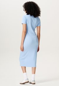 Light blue, short-sleeved, knee-length dress made of soft fabric. Features a fitted silhouette and subtle ribbed texture. Worn with white socks and casual shoes.