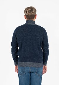 Maglione blu navy con una finitura testurizzata, dotato di un colletto alto e polsini e orlo a costine in grigio a contrasto. Si abbina a jeans di denim.